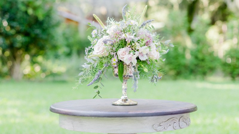 8 Flower bouquet in a silver vase on a round wooden table outdoors.