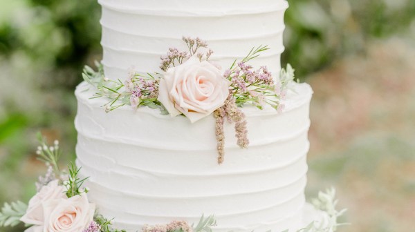 Three-tier white cake with pink roses and greenery decorations.