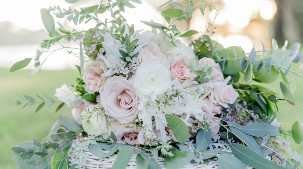 Floral bouquet with pink and white roses, greenery in a woven basket outdoors.