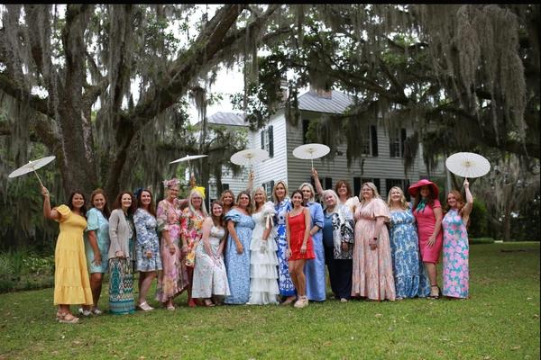 Group of women in colorful dresses holding parasols on a lawn.