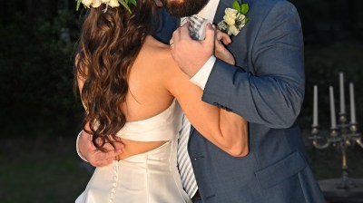 Bride and groom share an embrace outdoors under string lights.
