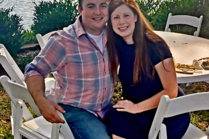 Couple sitting on white chairs near a lake, smiling at the camera.