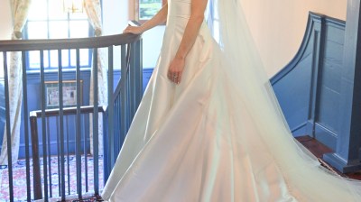 Bride in white gown with long train standing on staircase.
