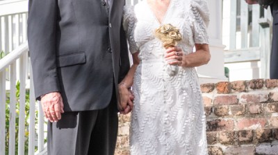 Couple holding hands in wedding attire standing on brick steps.