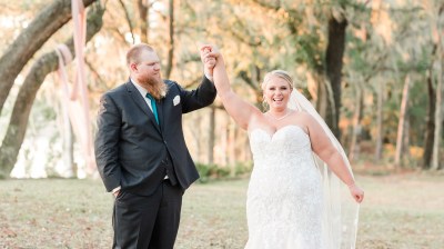 Bride and groom smiling under trees with draped fabric.
