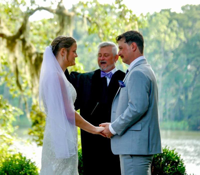 Bride and groom holding hands outdoors with officiant.