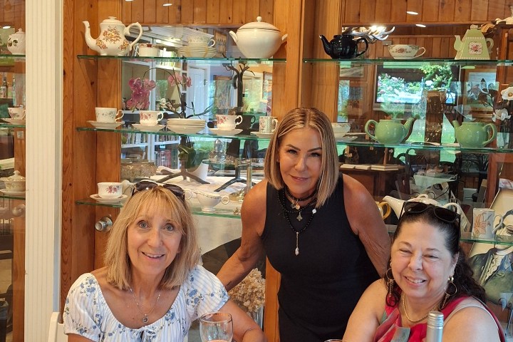 Three women enjoying a meal at a table with wine and snacks indoors.