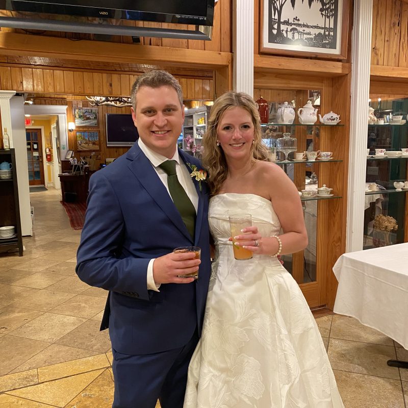 Couple in formal attire, holding drinks, smiling indoors.
