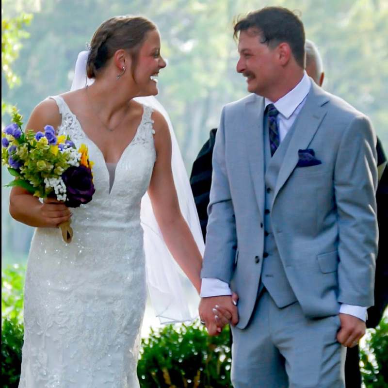 Bride and groom smiling and holding hands outdoors.