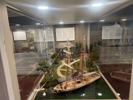 Glass display with a detailed ship model and miniature landscape inside.
