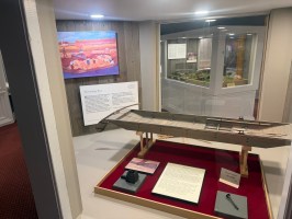 Museum display of a model boat, info panels, and artwork on a wall.