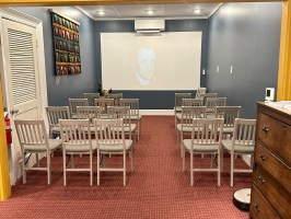 Room with rows of chairs facing a screen displaying a face.